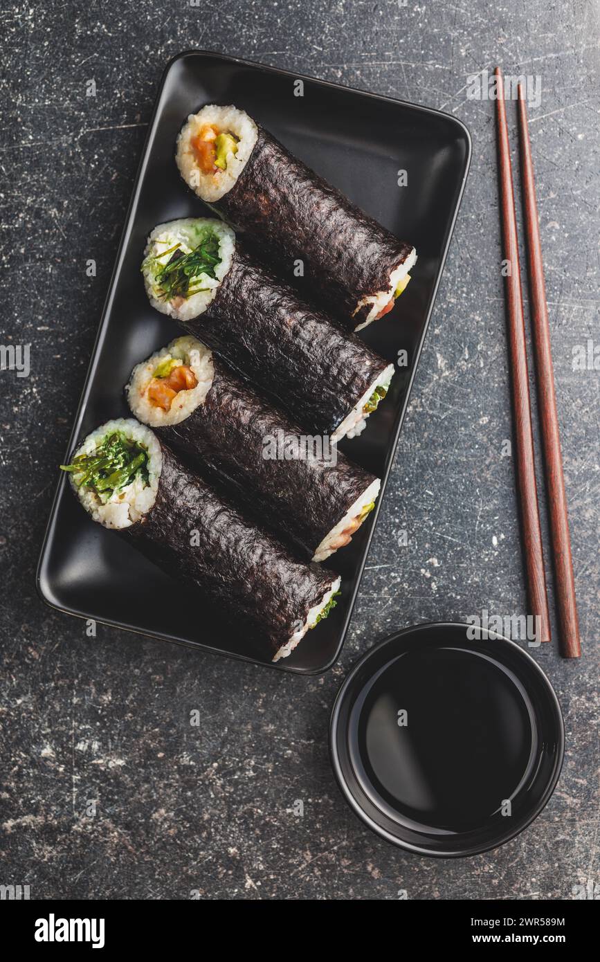 A black plate with sushi pieces with accompanying chopsticks and bowl of soy sauce. The sushi shows a variety of colors, textures, and fillings, showc Stock Photo