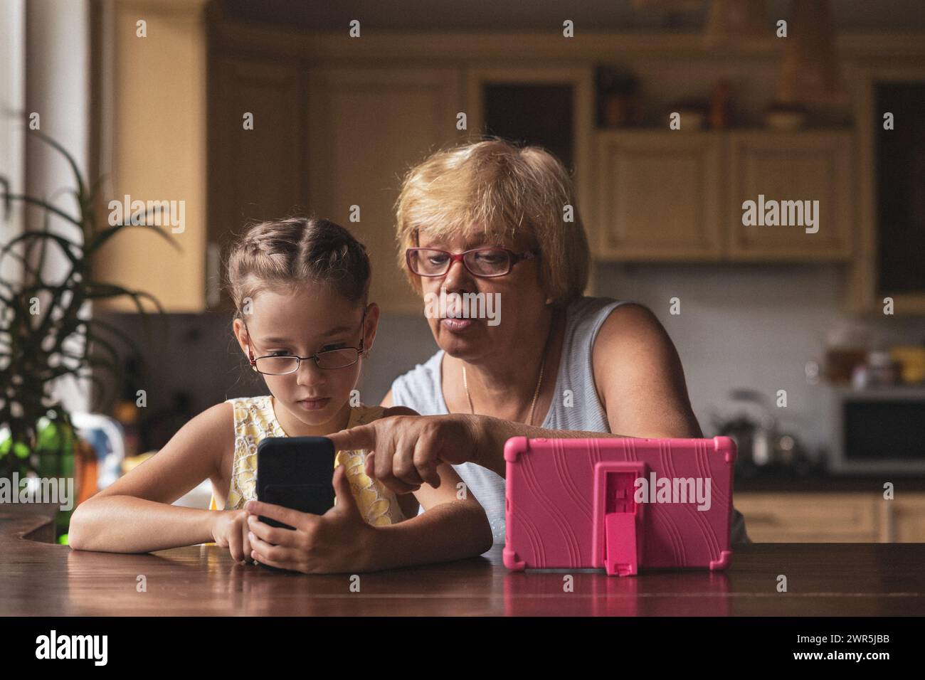 Girl and grandma with glasses sitting at the table with gadgets Stock Photo