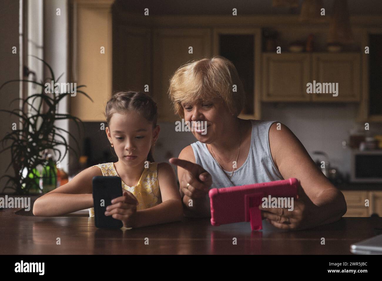 Grandma shows her granddaughter her phone in the kitchen Stock Photo