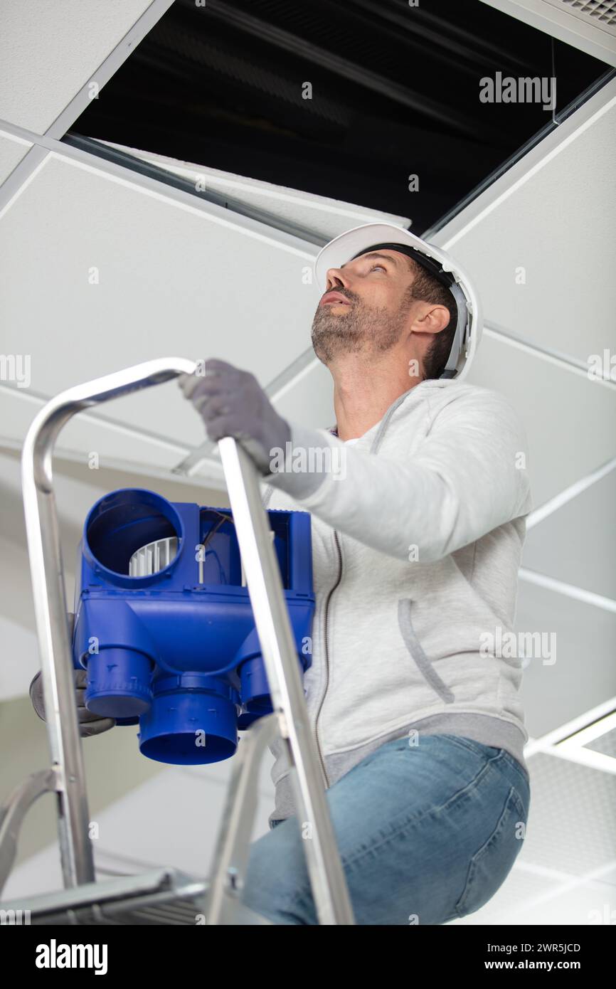 male electrician on stepladder installing ceiling device Stock Photo