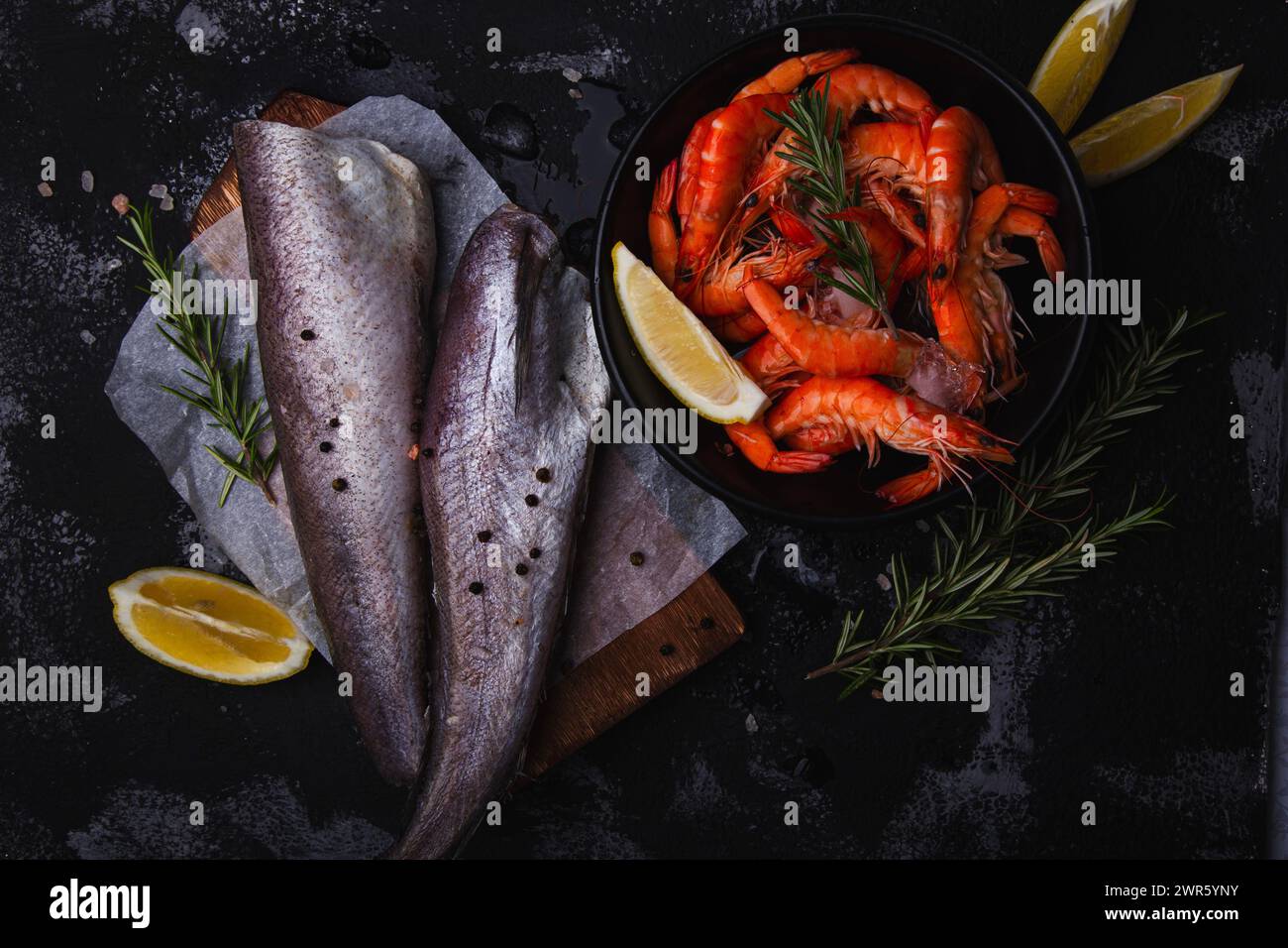 Fresh seafood arrangement with prawns and fish hake on dark background, ideal for culinary presentations. Stock Photo