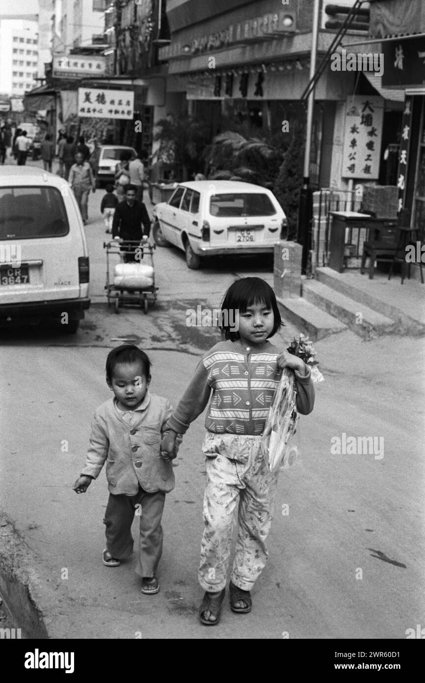 A local girl holding her younger brother's hand as they walk down a street in Tai Po, New Territories, Hong Kong, 1982 Stock Photo