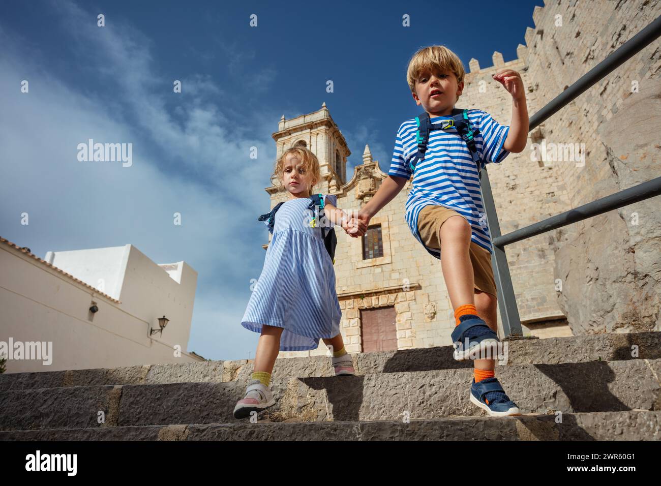 Kids boy and girl do sightseeing in Spain Peniscola old town going down the stairs with church of the Ermitana on background sunny hot day Stock Photo