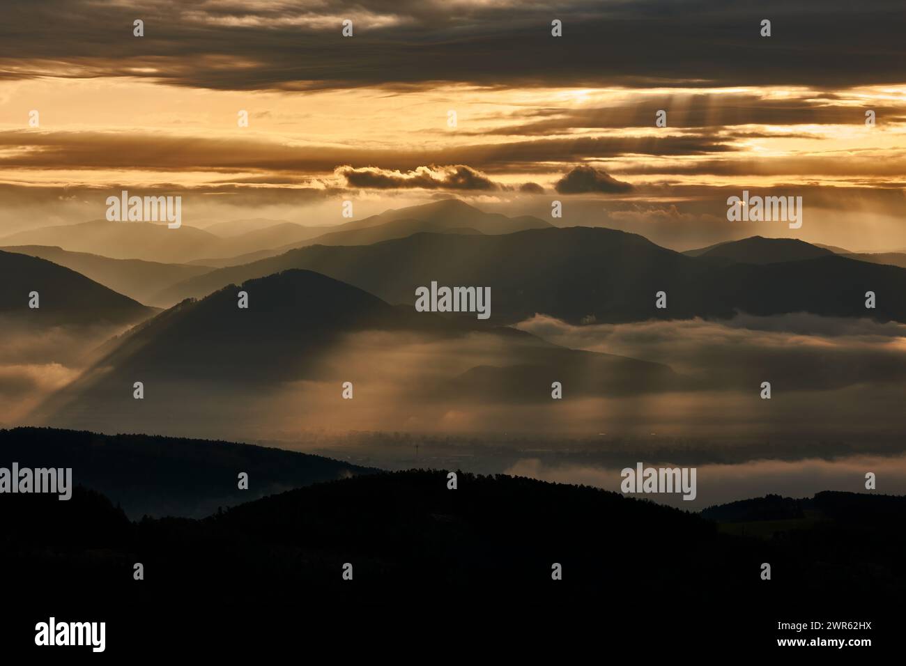 Mountain misty landscape at sunrise.The first beams of the sun shining through the colorful clouds. With silhouette of hills. Vrsatec, Slovakia Stock Photo