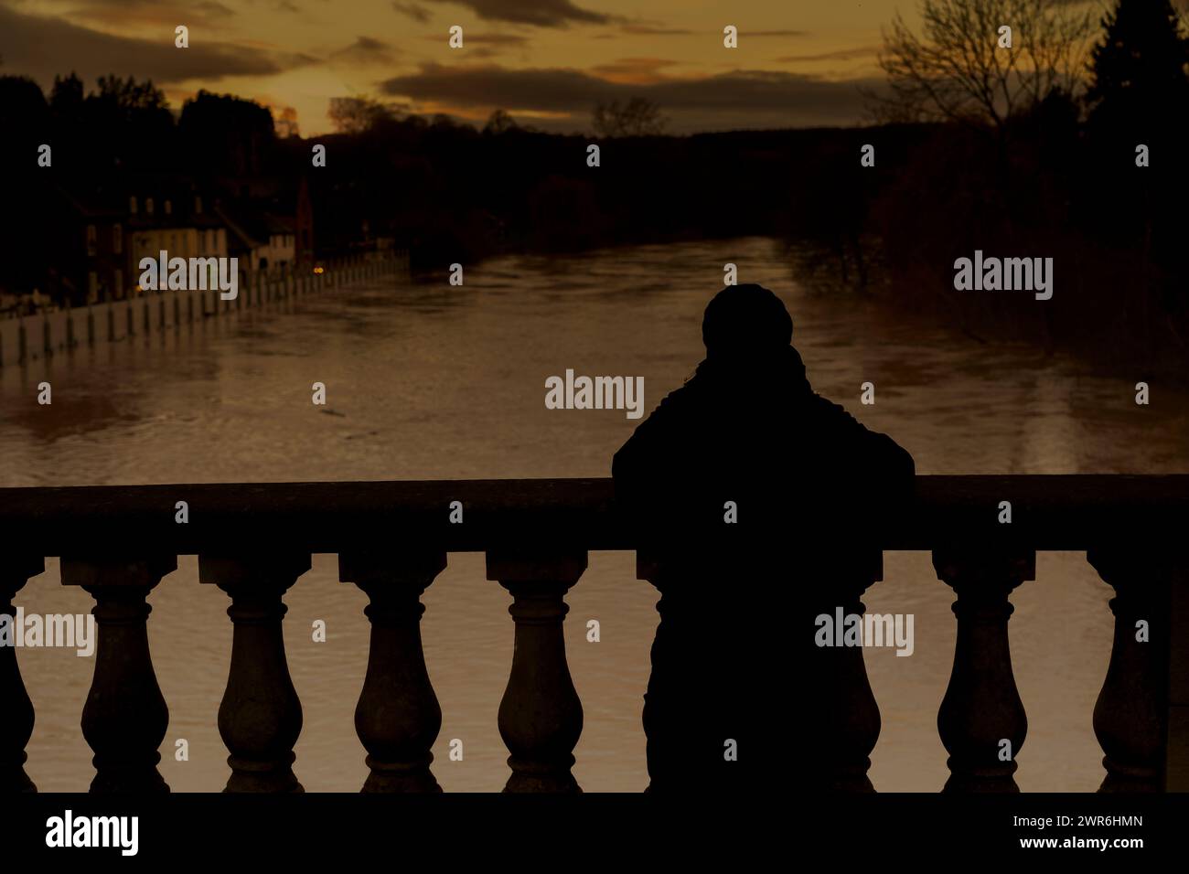 Rear view silhouette of person looking from Bewdley bridge at the River Severn below with its burst banks, being held back by town flood barriers. Stock Photo