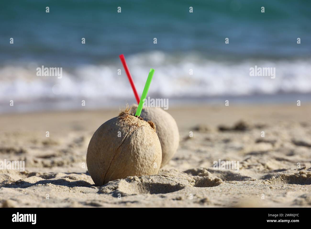 Coconut cocktails with straws on a sand of sea beach Stock Photo