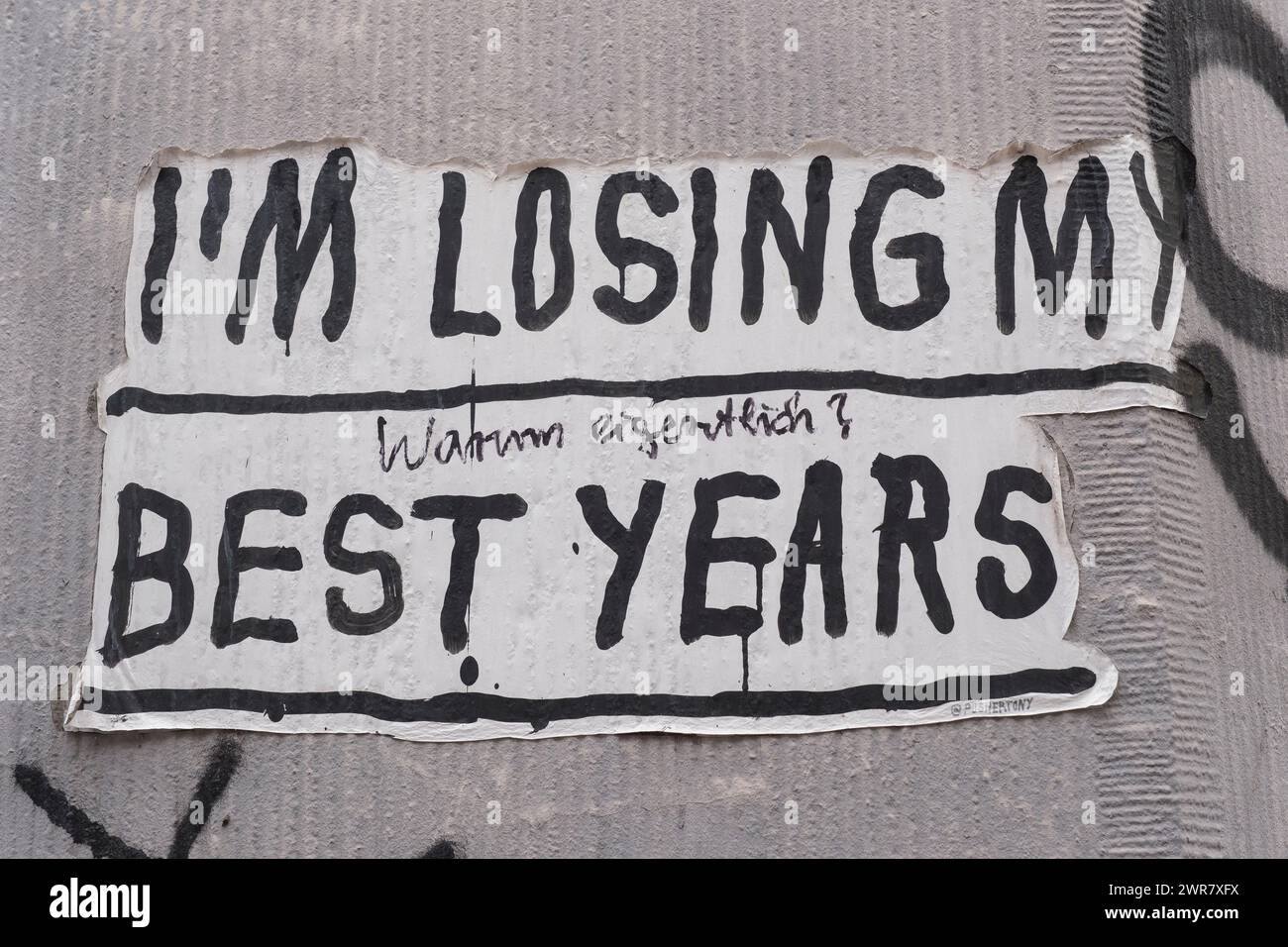 Street art in Körner Street: The slogan I am losing my best years printed on paper and stuck to a wall with a handwritten comment Why actually ? Stock Photo