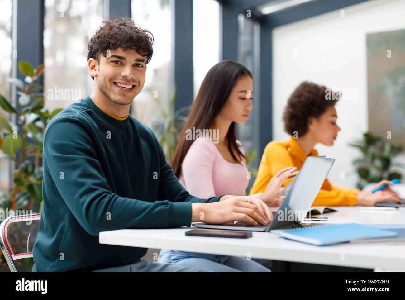 Cheerful latin male student with classmates using laptops Stock Photo ...