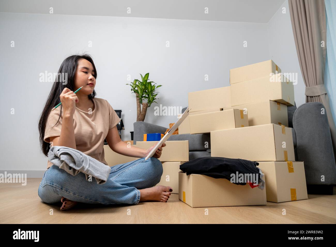 The young woman is checking a list of household items in a paper box to prepare for moving into a new hous Stock Photo