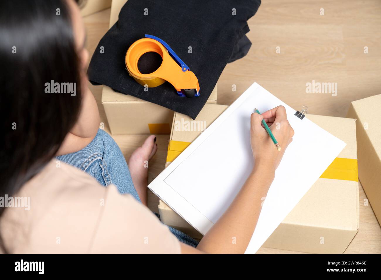 The young woman is checking a list of household items in a paper box to prepare for moving into a new hous Stock Photo