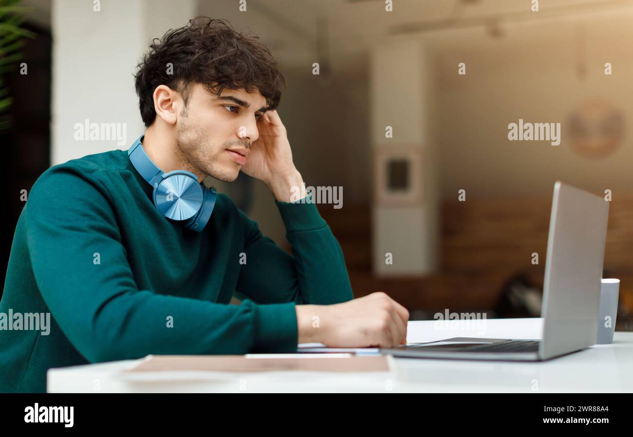 Pensive man student with headphones using laptop Stock Photo