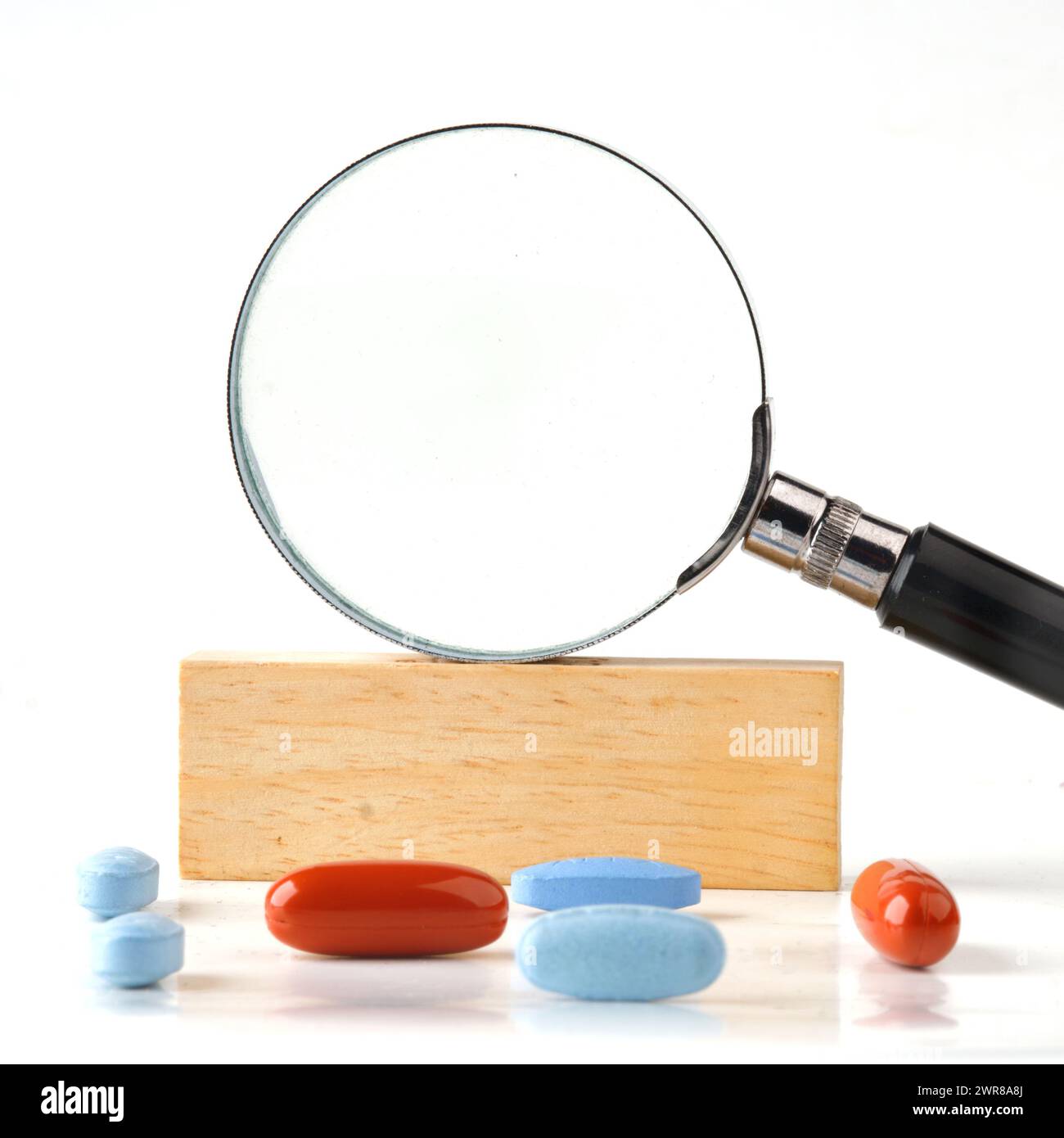 Magnifying glass on a wooden bar in close-up with pills in the foreground. A place to c Stock Photo