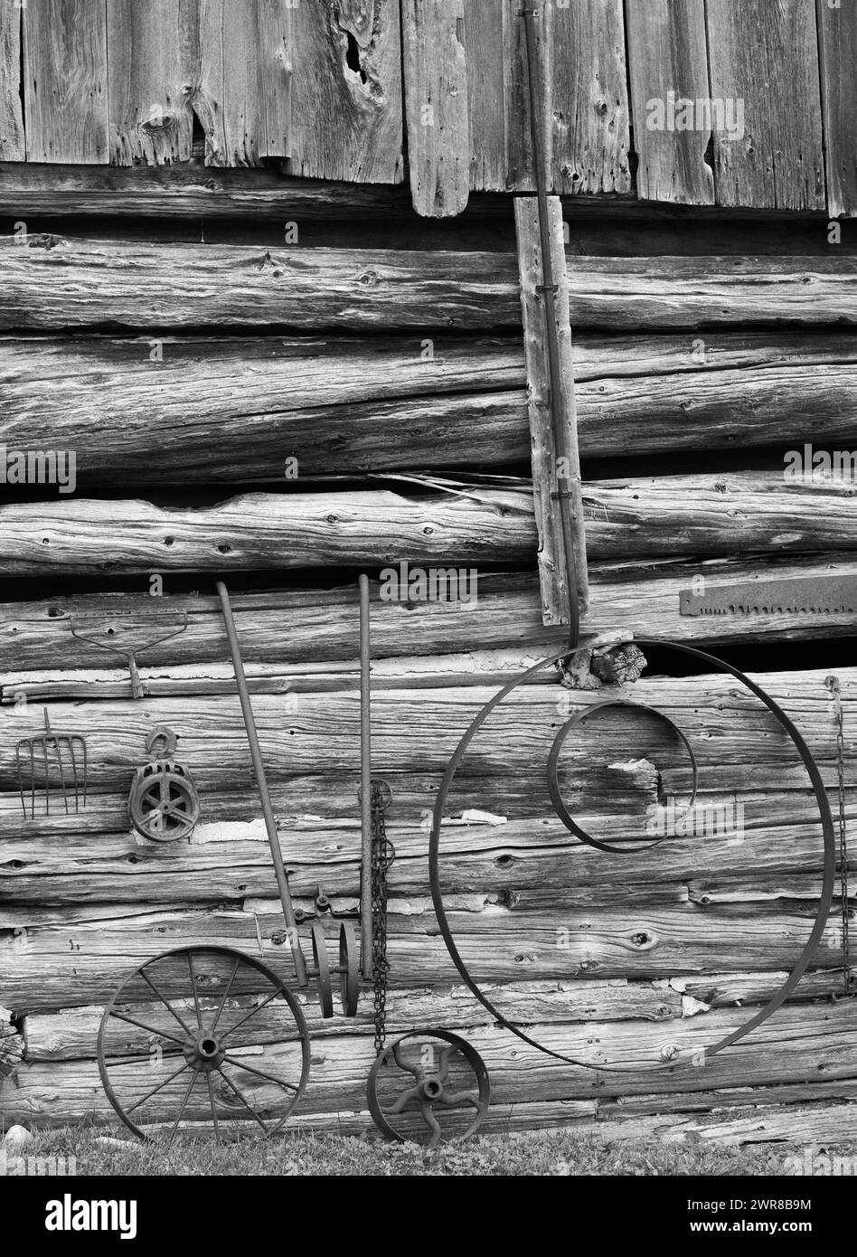 Old antique rustic rusty farm machinery in front of log cabin exterior wall of shed on rural farm in the countryside chinked log wall black and white Stock Photo