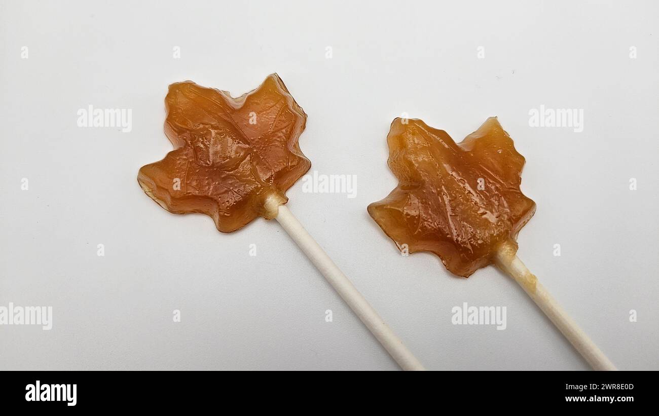 Two maple leave-shaped candies made with brown sugar coating on white sticks, displayed on a table Stock Photo
