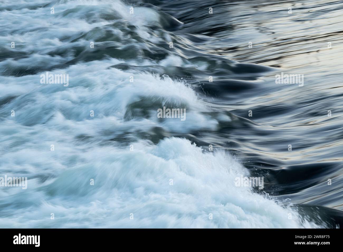 Rapid water flow over barrier with silky surface, river overflow over dam close up with splash and foam, abstract landscape pastel blue Stock Photo
