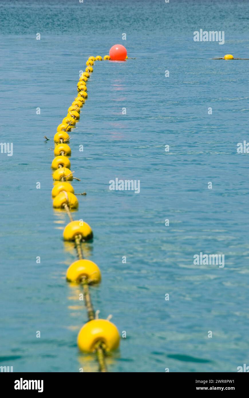 A line of buoys floating near a single buoy in the water Stock Photo