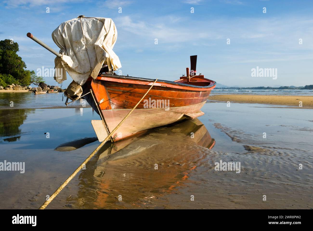 A wooden boat rests on the sandy shore beside the water Stock Photo