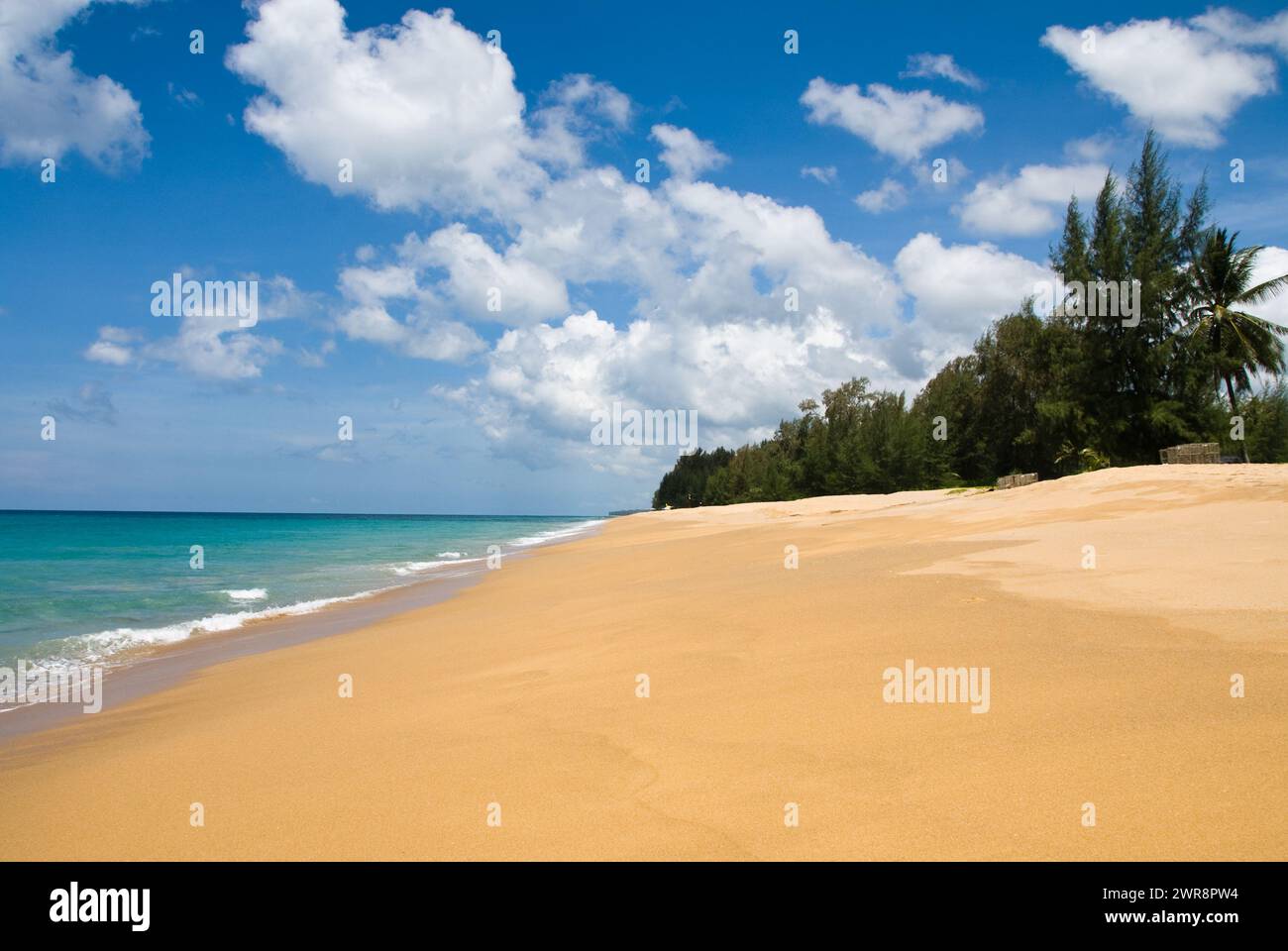 Deserted sandy beach by the clear ocean under a blue sky with clouds Stock Photo
