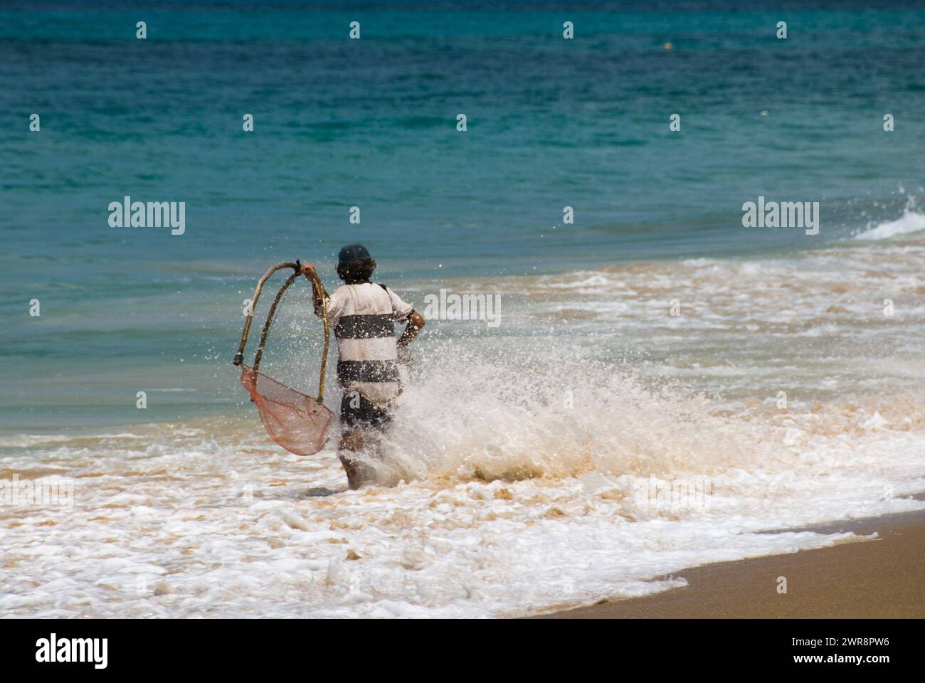 A man with a surfboard and harness entering the ocean Stock Photo