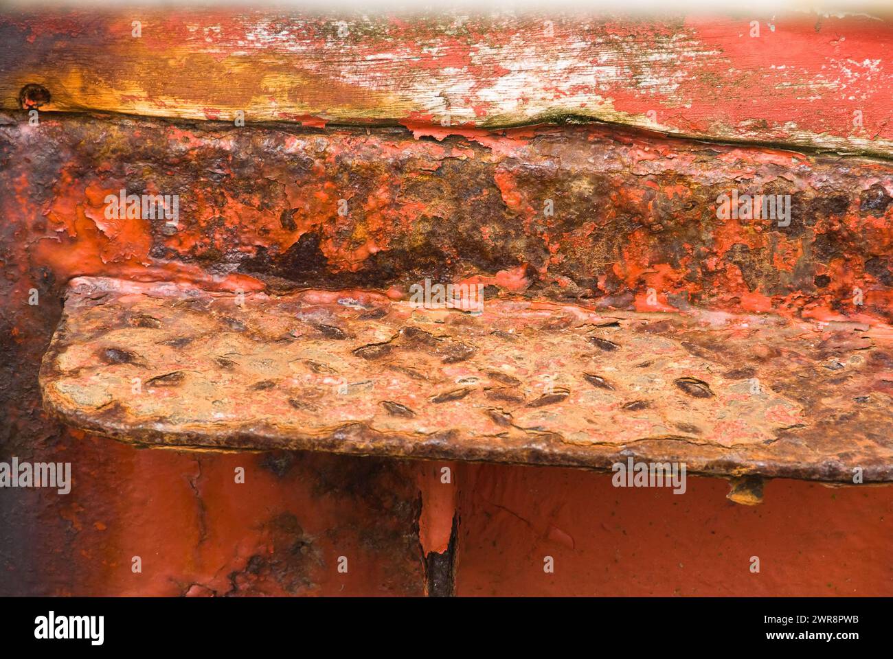 Orange painted metal bench against a rusty wall Stock Photo