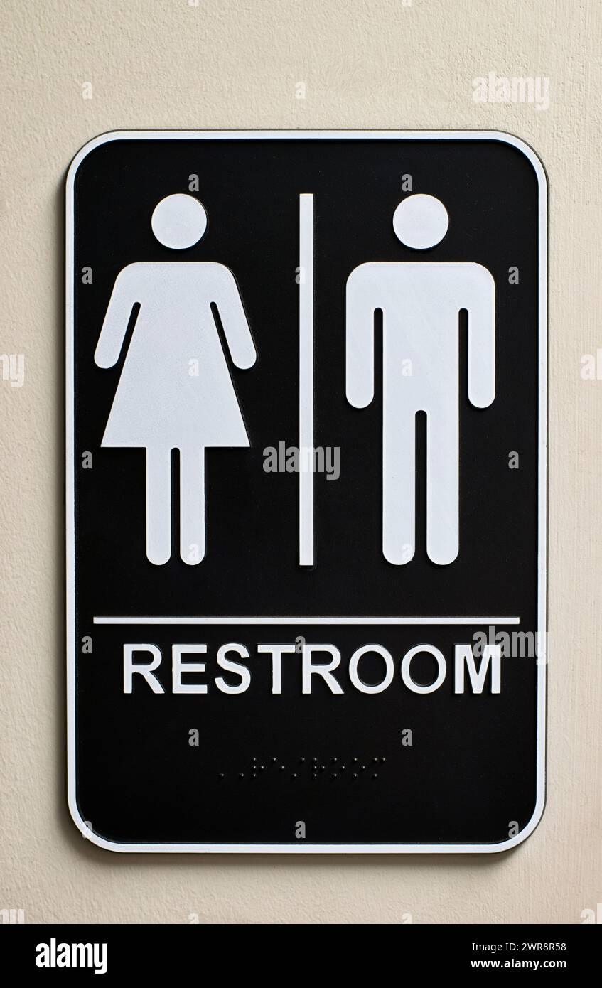 Unisex bathroom sign on a wall with male and female icons, braille at the bottom and no handicap icon. Men and women's bathroom, vertical format image. Stock Photo