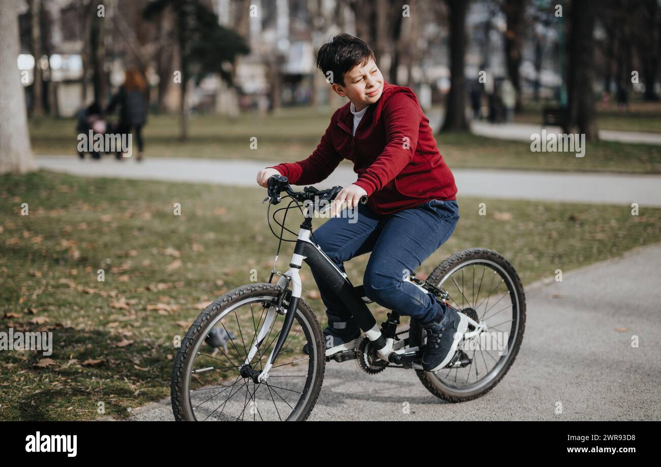 Young boy enjoying a leisurely bike ride in an urban park with greenery ...
