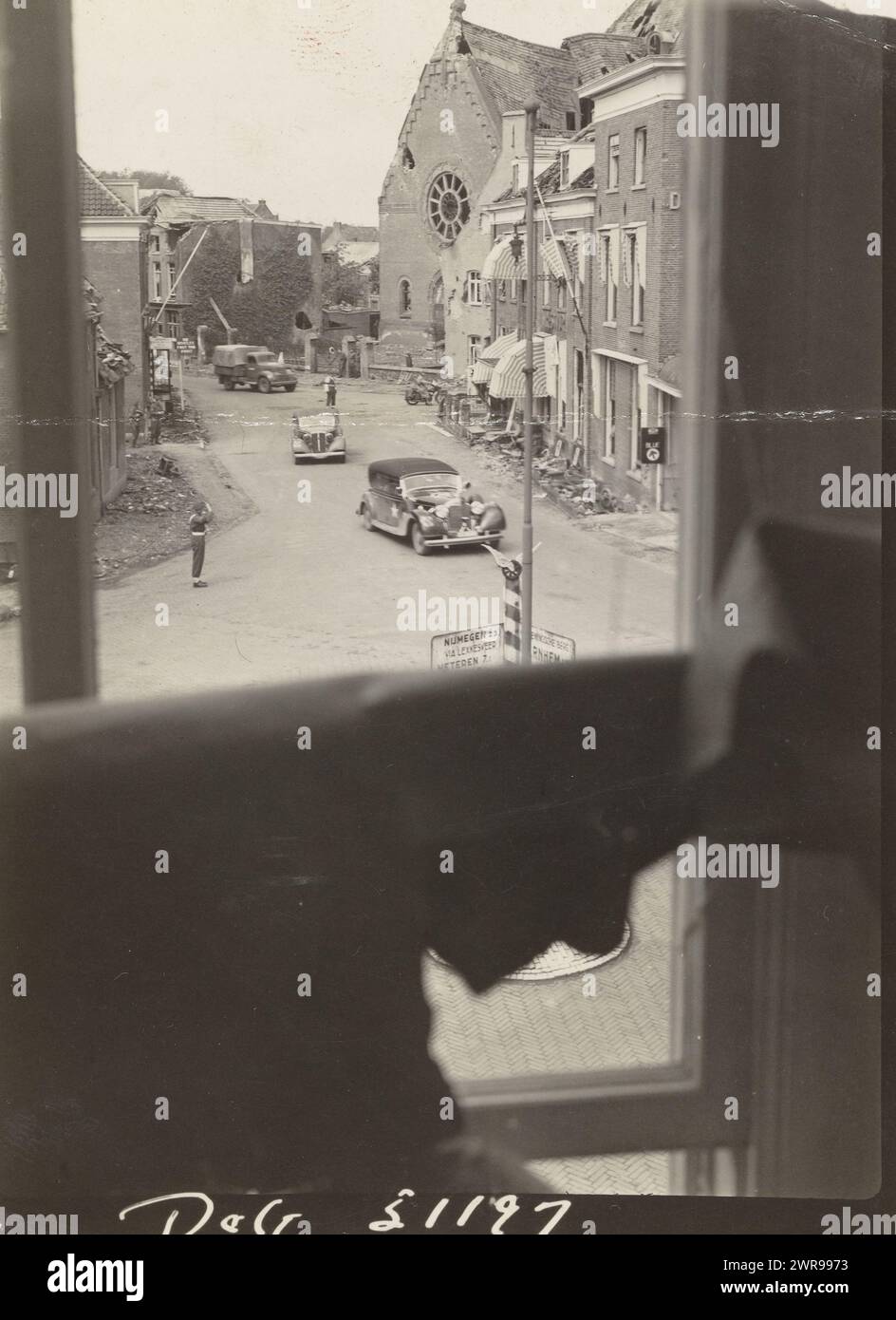 Destruction in a city, View of a street with destroyed buildings from a window. There are a few cars driving in the street and a suspect. English soldier seen saluting., anonymous, Netherlands, 1940 - 1950, photographic support, height 11 cm × width 8 cm, photograph Stock Photo