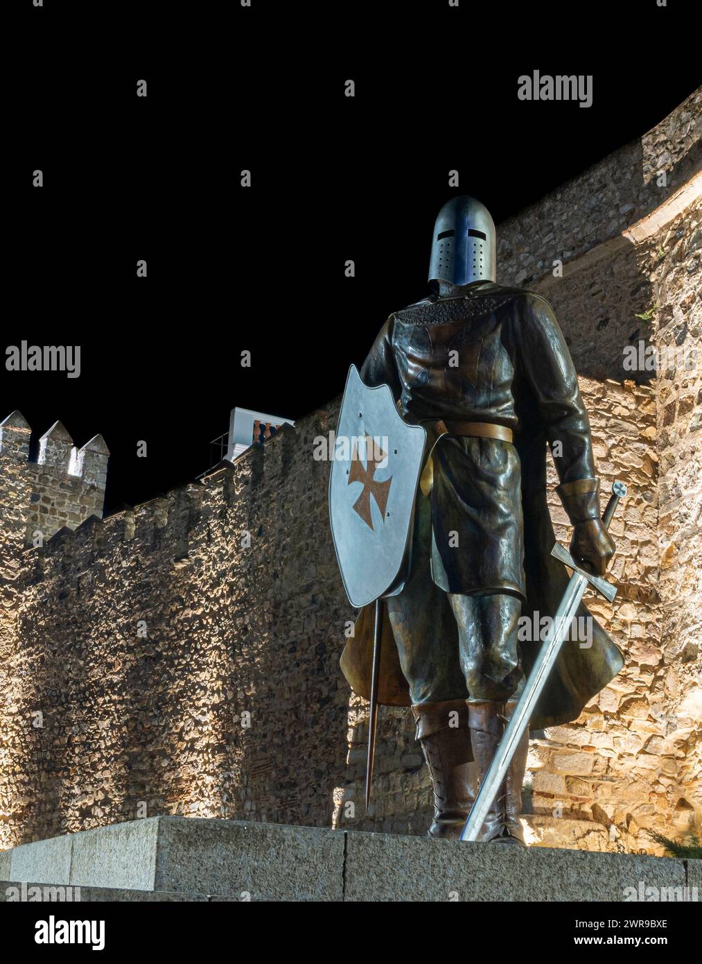 A statue of a warrior with two swords and a helmet in front of a stone wall Stock Photo