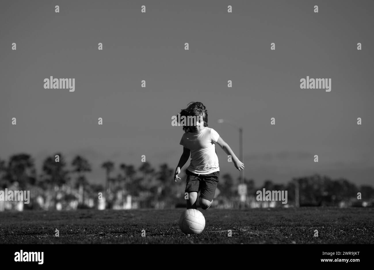 Little kid boy playing football in the field with soccer ball. Kids