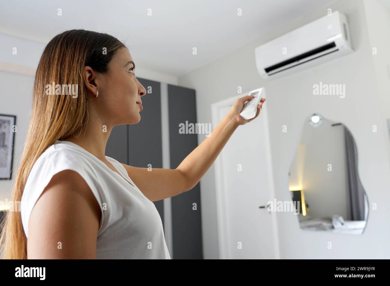 Portrait of young woman using air conditioner remote control to lower