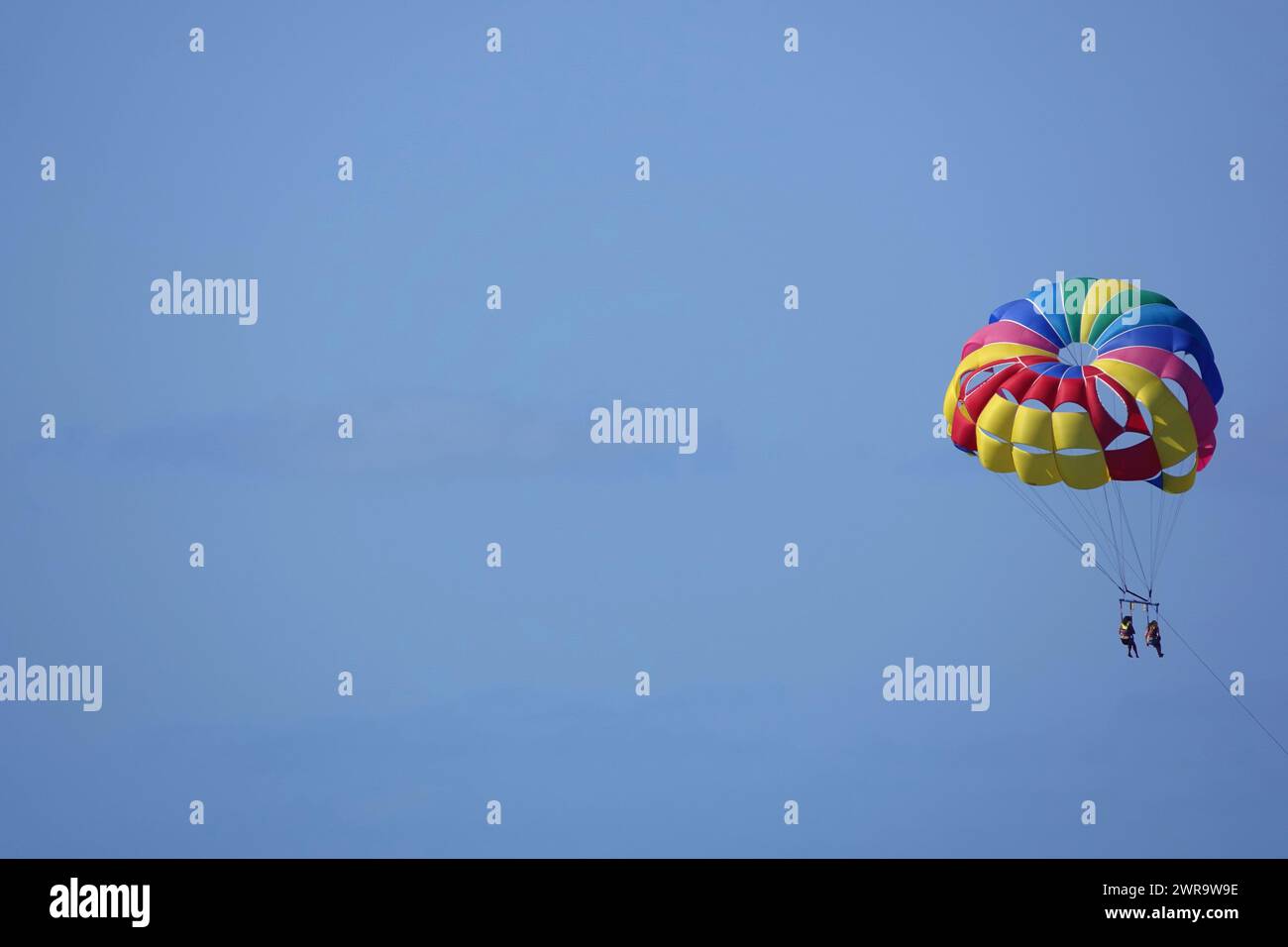 Two people parasailing against a clear bright blue sky Stock Photo