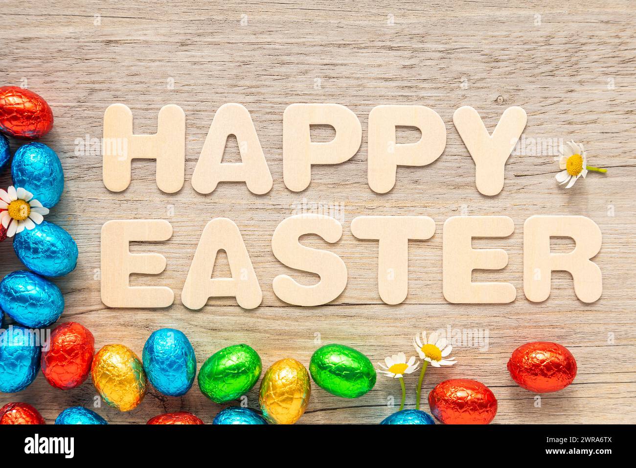 Chocolate, foil covered Easter eggs on wooden background with the text "Happy Easter". Stock Photo