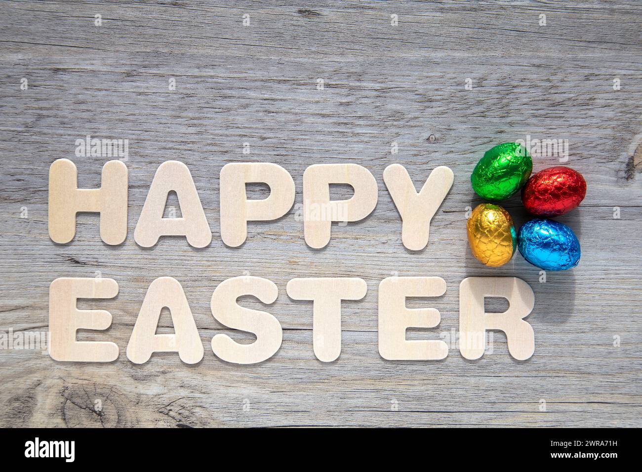 Foil covered Easter eggs on wooden background with the text "Happy Easter". Stock Photo