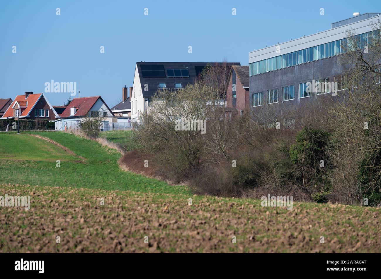 Zellik, Flemish Brabant, Belgium March 8, 2024 - Hills and farmland with industrial buildings in the background Stock Photo