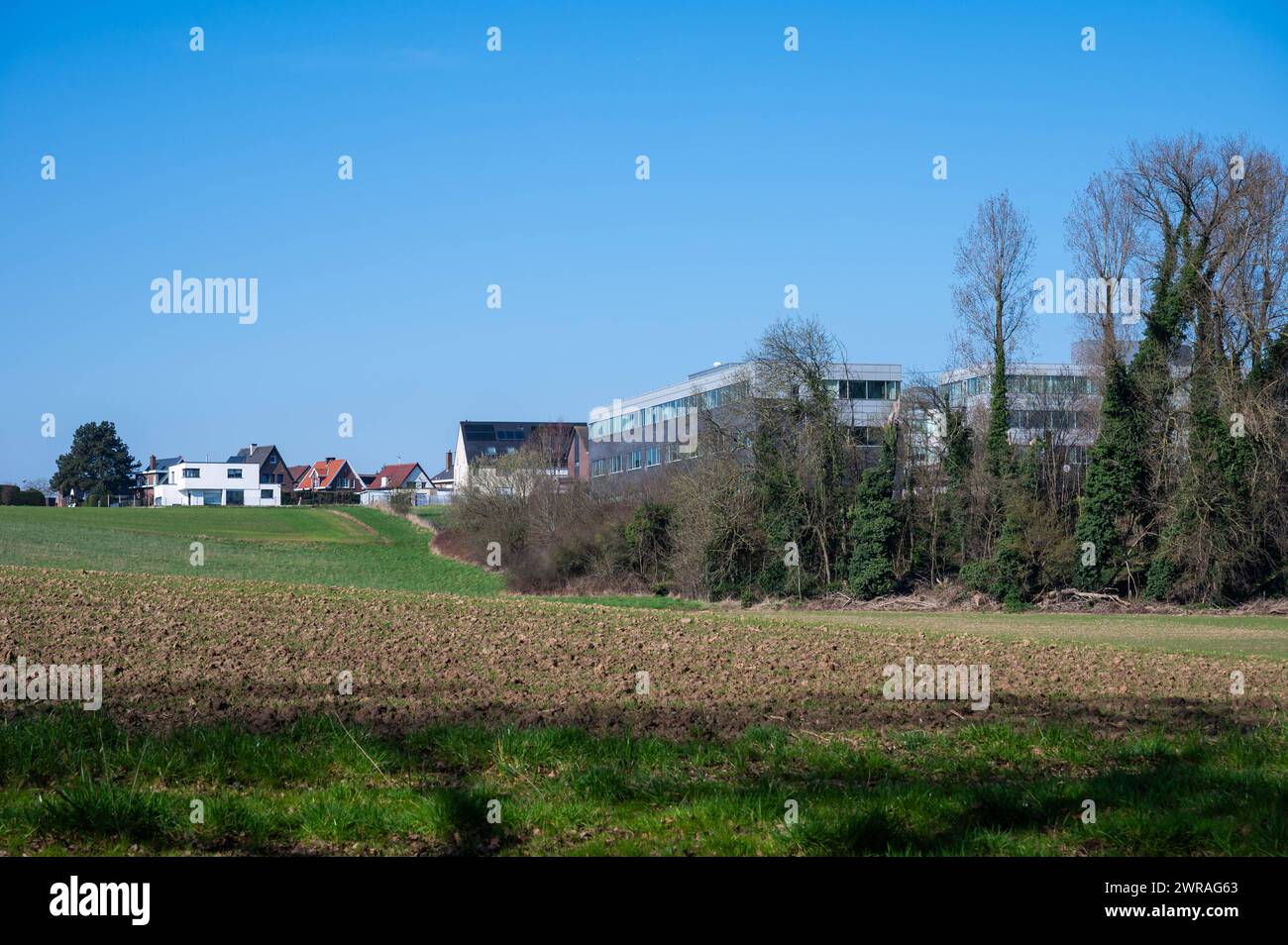 Zellik, Flemish Brabant, Belgium March 8, 2024 - Hills and farmland with industrial buildings in the background Stock Photo