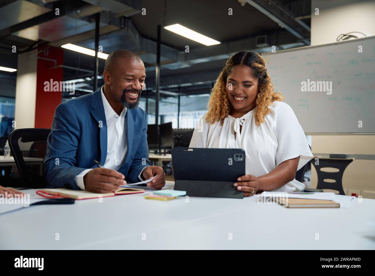 Three happy multiracial colleagues looking down and smiling while using digital tablet in office Stock Photo