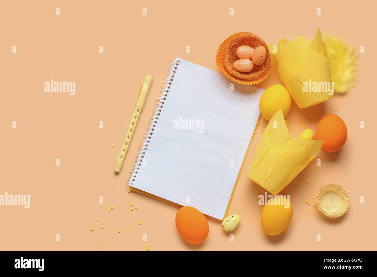 Blank notepad for recipes with pen, Easter eggs and baking molds on orange background Stock Photo