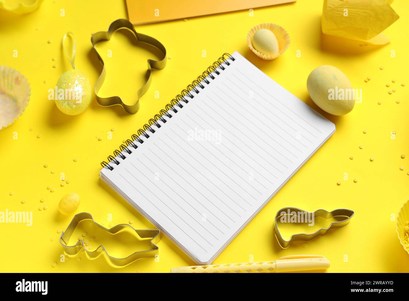 Blank notepad for recipes with pen, Easter eggs and baking tools on yellow background Stock Photo