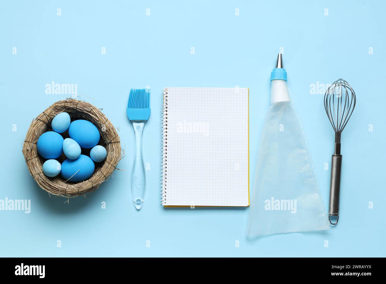 Blank notepad for recipes, baking tools and nest with Easter eggs on blue background Stock Photo