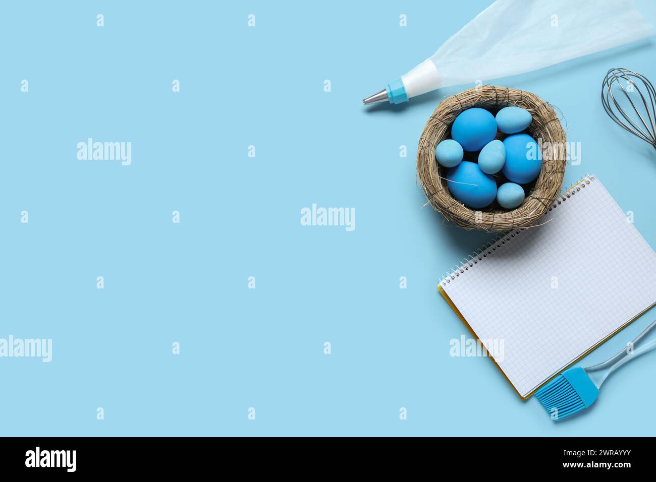 Blank notepad for recipes, baking tools and nest with Easter eggs on blue background Stock Photo
