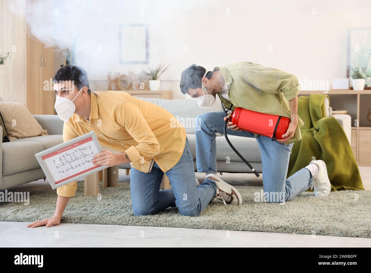 Young men with evacuation plan and fire extinguisher in burning building Stock Photo