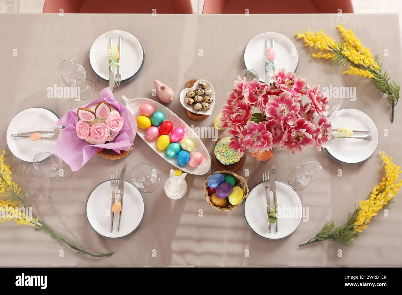 Festive stylish table setting with mimosa flowers, Easter cake and painted eggs Stock Photo