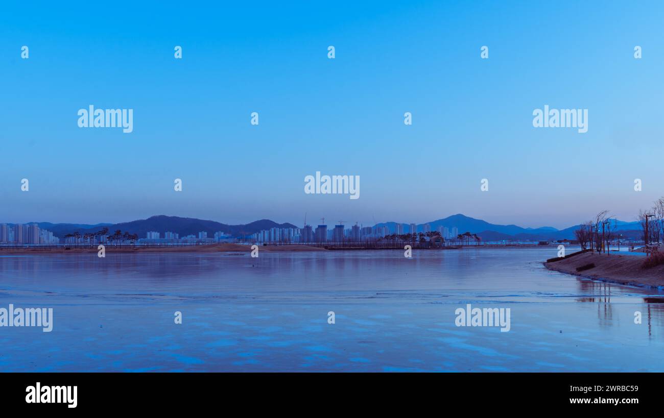 Twilight cityscape with a calm river partially covered in ice, reflecting blue hues, in South Korea Stock Photo