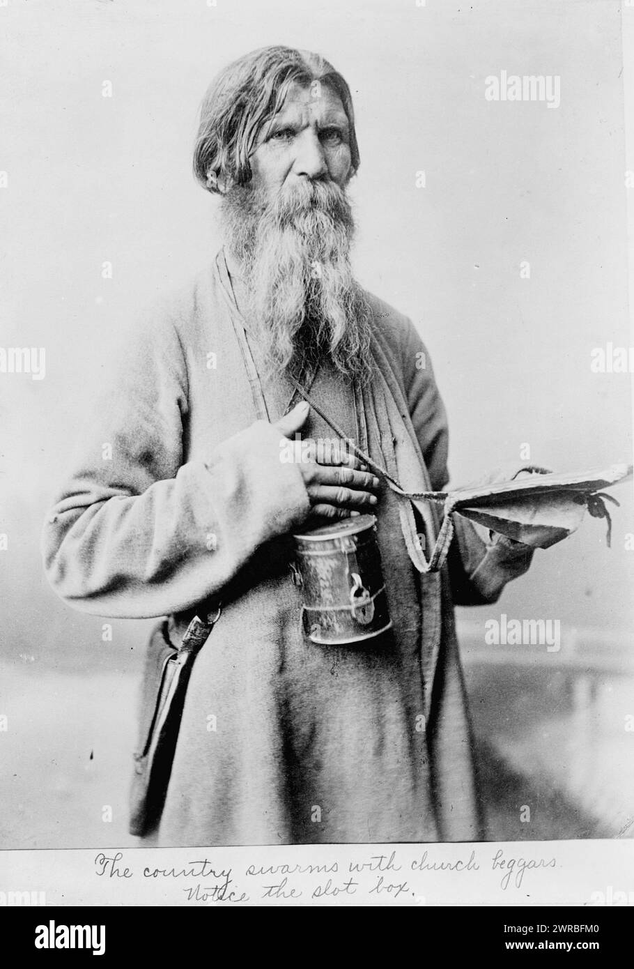 The Country swarms with church beggars, Bearded man, standing, three-quarter length, with box with slot to deposit money, Russia., between ca. 1880 and 1924, Beggars, Russia, 1880-1930, Photographic prints, 1880-1930., Portrait photographs, 1880-1930, Photographic prints, 1880-1930, 1 photographic print Stock Photo