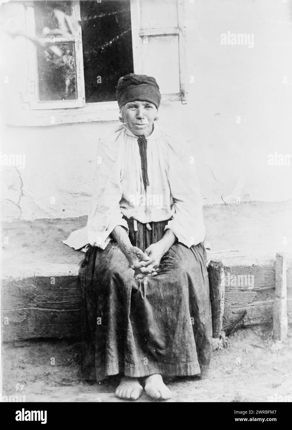 Old woman seated, outside house, full-length, Russia, between ca. 1880 and 1924, Women, Clothing & dress, Russia, 1880-1930, Photographic prints, 1880-1930., Portrait photographs, 1880-1930, Photographic prints, 1880-1930, 1 photographic print Stock Photo