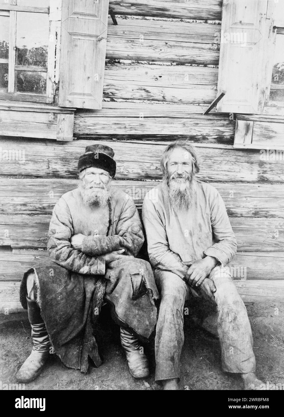 Two men seated, outside of log house, full-length, Russia, M. Dmitrievʹ., 1895?, Men, Clothing & dress, Russia, 1890-1900, Photographic prints, 1890-1900., Portrait photographs, 1890-1900, Photographic prints, 1890-1900, 1 photographic print Stock Photo