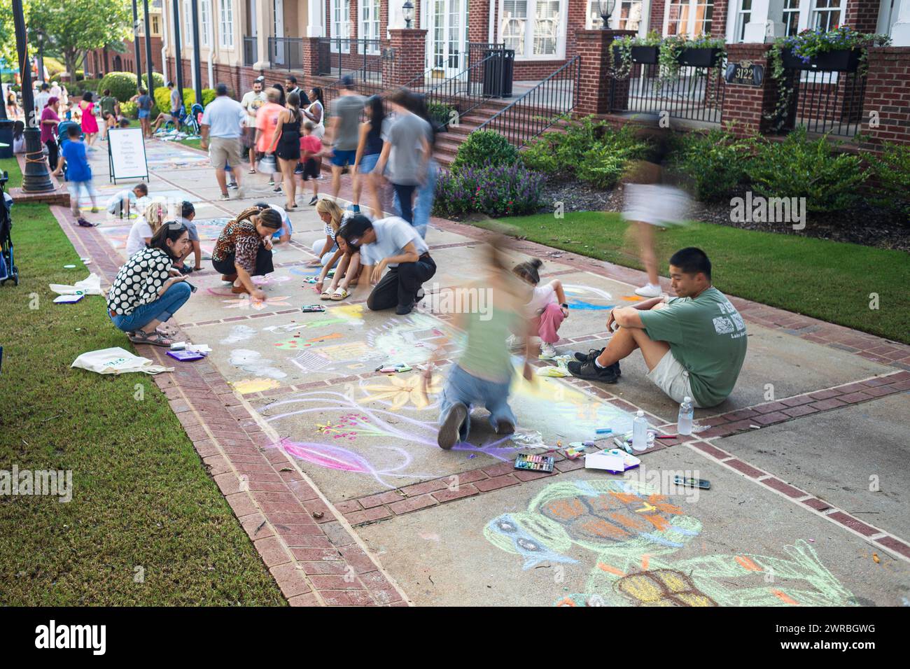 Duluth, GA / USA – August 11, 2023:  Motion blur of people drawing artwork on a sidewalk as they participate in a local chalk art festival. Stock Photo