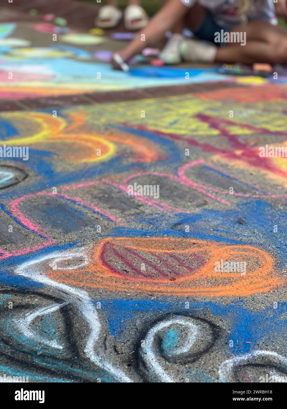 The sidewalk of a public park is covered with colorful chalk art at a locak chalk art festival. Stock Photo