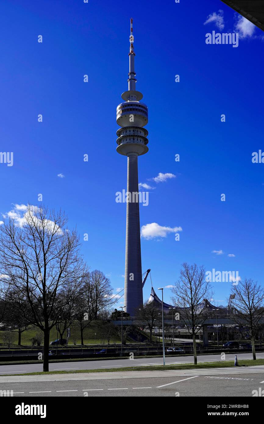 A tall television tower rises into the blue sky with trees in the foreground, BMW WELT, Munich, Germany Stock Photo