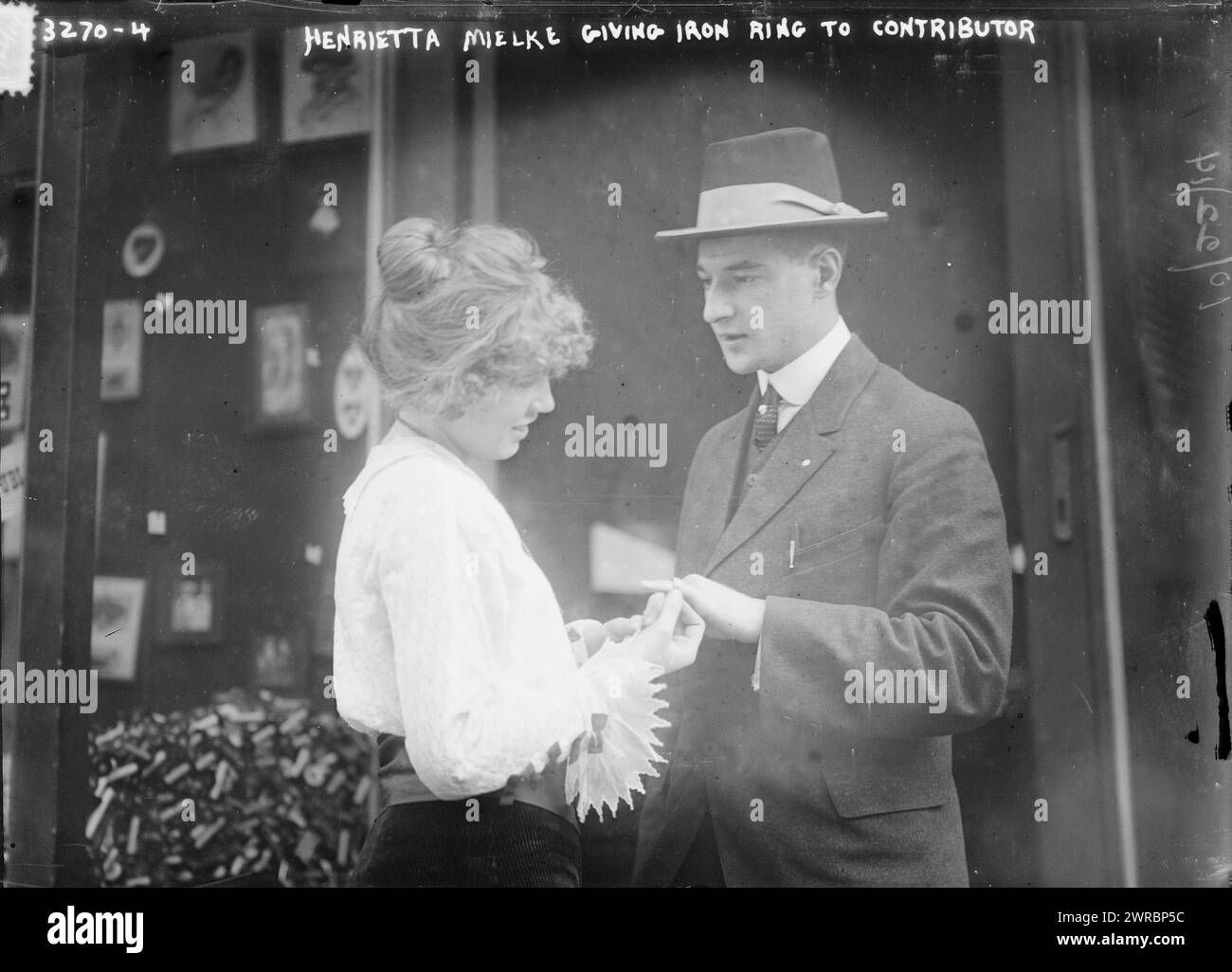 Henrietta Mielke giving iron ring to contributor, Photograph shows Henrietta Mielke (b. 1897) giving a ring to a man. Her father, Henry Mielke was a store owner and member of the 'Gold for Iron' (Gold fur Eisen) organization which gave iron rings to people in exchange for gold and jewels which were used to support the German war effort during World War I. Photograph probably taken outside? Mielke's store located on Second Avenue at the corner of 87th Street in New York City., 1914 Oct. 22, World War, 1914-1918, Glass negatives Stock Photo